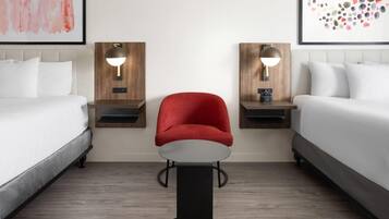 A hotel room with two beds, a red chair, a small table, and two wall-mounted lamps.