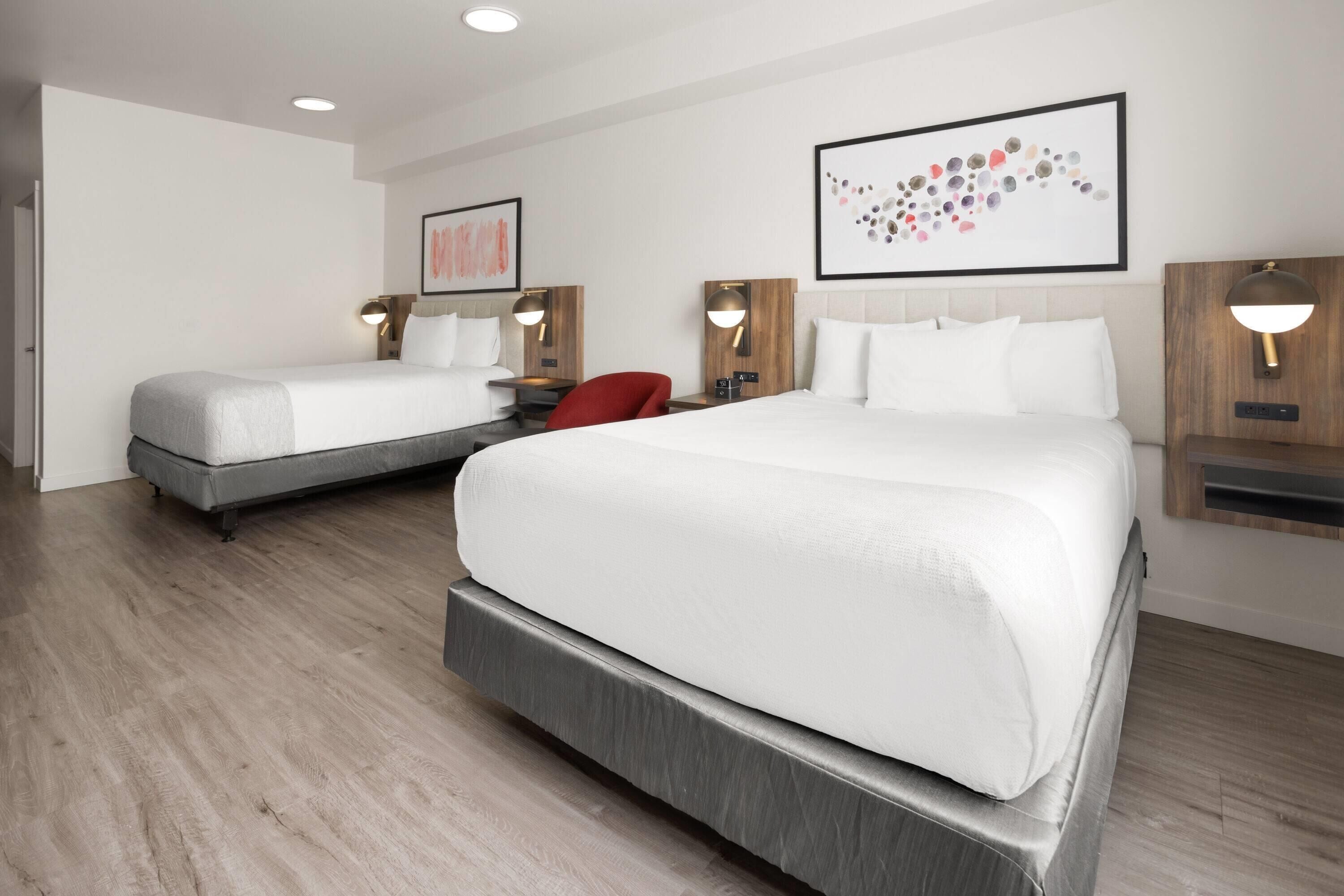 Habitación de hotel con dos camas, una silla roja y lámparas fijadas a la pared.