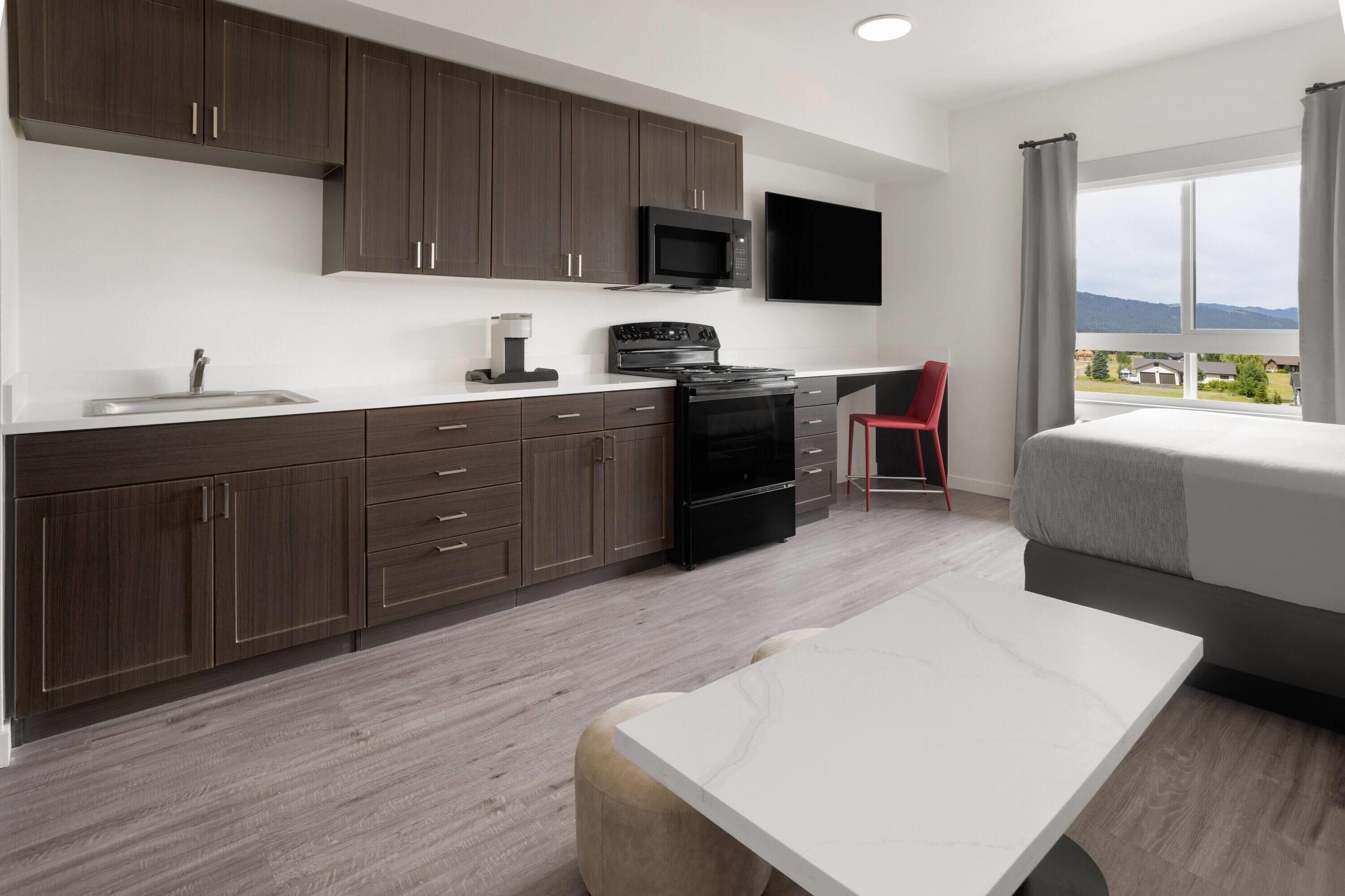 A modern kitchen with dark wood cabinets, a microwave, stove, and a dining area with a white table and red chair.
