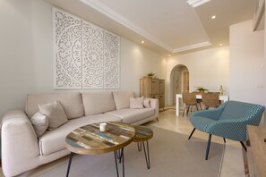 A modern living room with a sofa, two round coffee tables, a patterned armchair, and a decorative wall panel. - Apartment 'Jardines De Don Carlos' with Shared Pool, Wi-Fi and Air Conditioning (Marbella)