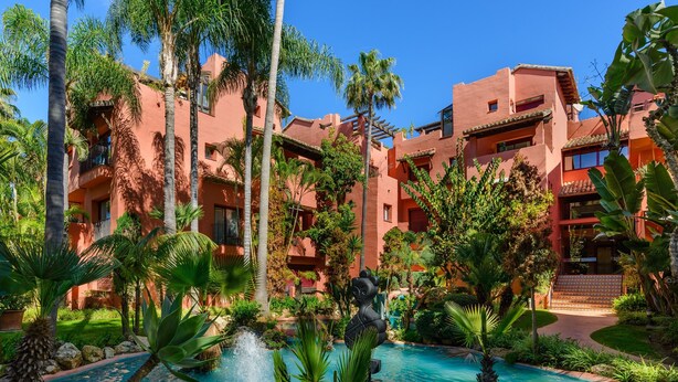 A hotel with a pool surrounded by palm trees and a statue.