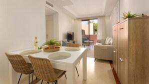 A modern living room with a white sofa, a dining table with wicker chairs, and a wooden cabinet.