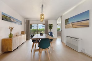 A modern dining area with a wooden table, chairs, a hanging light fixture, and artwork on the walls.