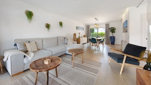 A modern living room with a sofa, two round wooden tables, a dark armchair, and a dining area in the background. - Villa 'Casa Giorianna - Luxury' with Shared Pool, Wi-Fi and Air Conditioning (Luz de Tavira)