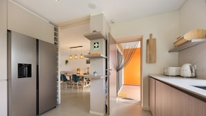 A modern kitchen with a built-in refrigerator, a dining area with chairs, and a kitchen counter with appliances. - Villa 'Casa Giorianna - Luxury' with Shared Pool, Wi-Fi and Air Conditioning (Luz de Tavira)