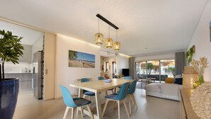 A modern dining area with a wooden table and blue chairs, a kitchen in the background, and a large window with a view. - Villa 'Casa Giorianna - Luxury' with Shared Pool, Wi-Fi and Air Conditioning (Luz de Tavira)