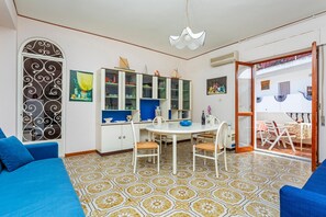 Un coin repas avec une table et des chaises blanches, un canapé bleu et un sol à motifs.