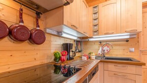A kitchen with wooden cabinets, a stainless steel sink, and a countertop with various kitchen utensils and a bowl of vegetables. - Chalet 'Ground Floor 110 m² – Very Close to the Slopes' with Mountain View, Private Terrace & Wi-Fi (Fontcouverte-la-Toussuire)