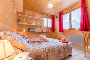 Een houten kamer met een bed, planken, een radiator en een raam met gordijnen.