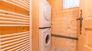 A compact laundry room with wooden walls, a stacked washer and dryer, and a metal handrail. - Chalet 'Ground Floor 110 m² – Very Close to the Slopes' with Mountain View, Private Terrace & Wi-Fi (Fontcouverte-la-Toussuire)
