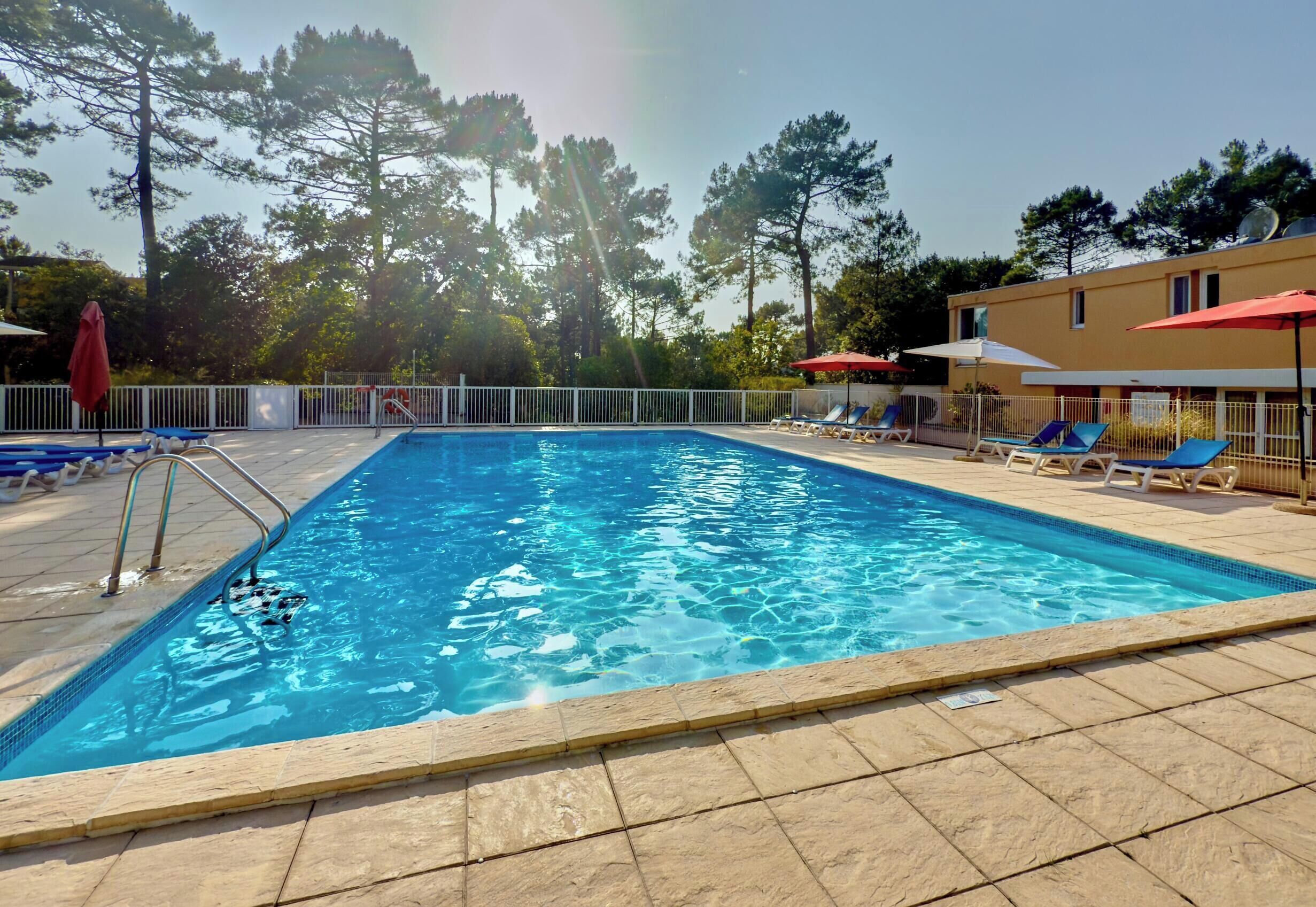 A swimming pool with a tiled deck, lounge chairs, and a white fence.