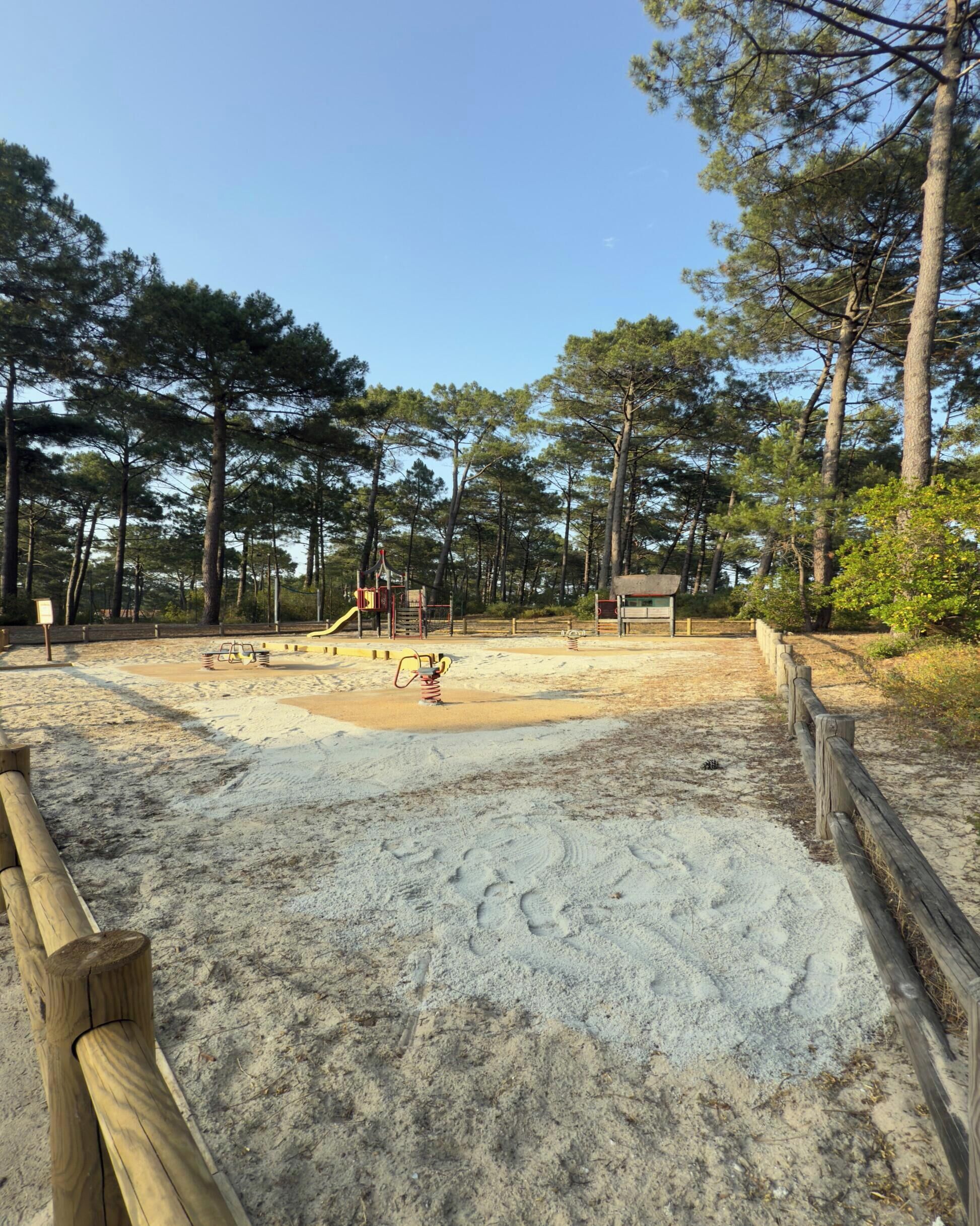 Une zone de plage sablonneuse avec une aire de jeux, entourée d’arbres.