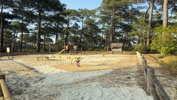 Une zone de plage sablonneuse avec une aire de jeux, entourée d’arbres.