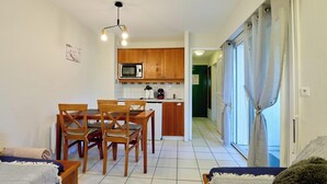 A compact living space with a dining area, kitchenette, and a view through a door. - Cozy apartment between lake and ocean – Terrace & shared pool in Carcans-Maubuisson (Carcans)