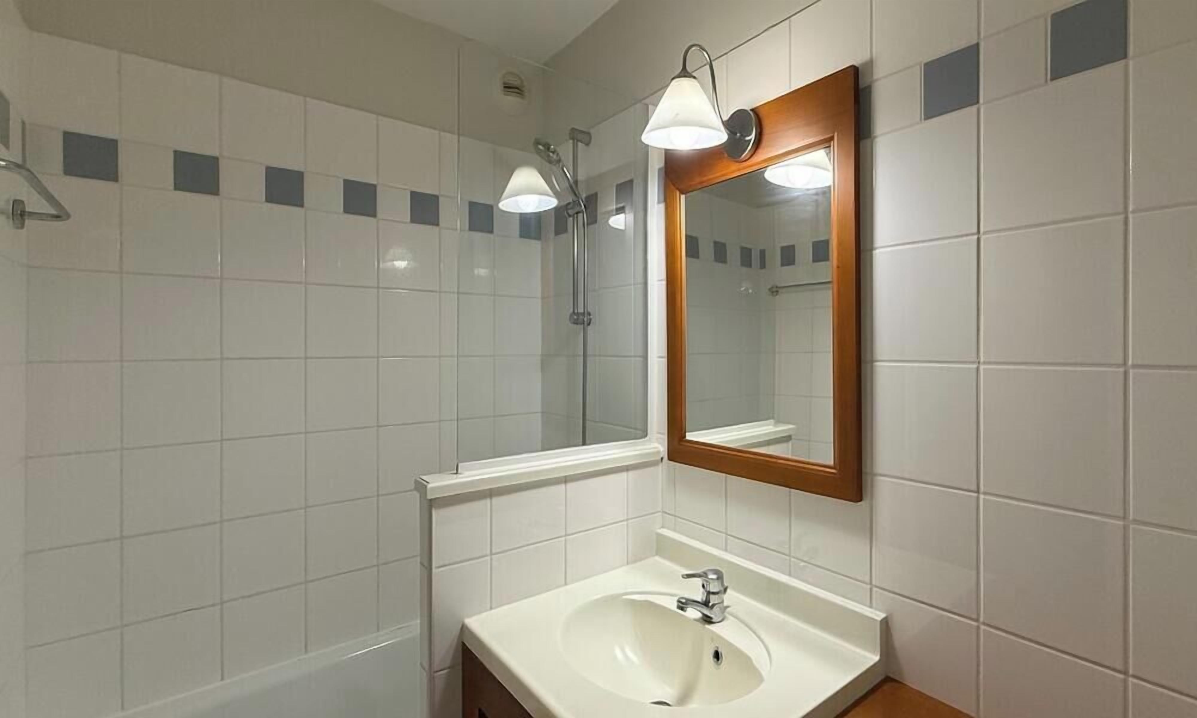 Een badkamer met witte tegels, een wastafel met spiegel en een douche.