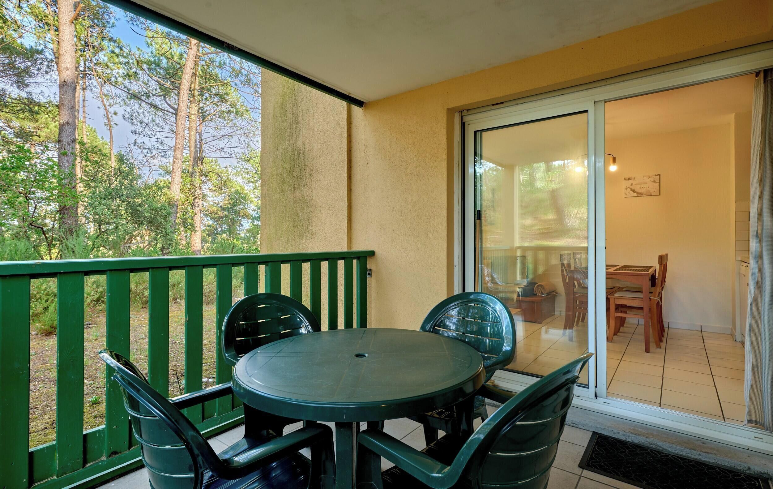 Un balcon avec une table et des chaises, une porte-fenêtre coulissante donnant sur un coin repas et une vue sur les arbres.
