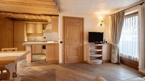 A wooden interior with a dining area, kitchen, TV, and a window with curtains.