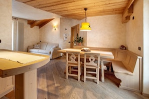 Un interior de madera con una mesa de comedor, sillas, un sofá, una planta en maceta y una lámpara colgante.