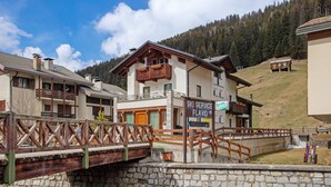 A ski service building with a wooden balcony, stone bridge, and a mountainous backdrop.