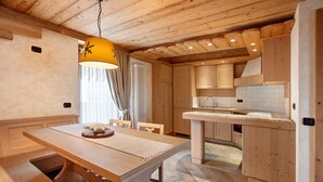 A wooden interior with a dining table, chairs, a hanging light fixture, and a kitchen area.
