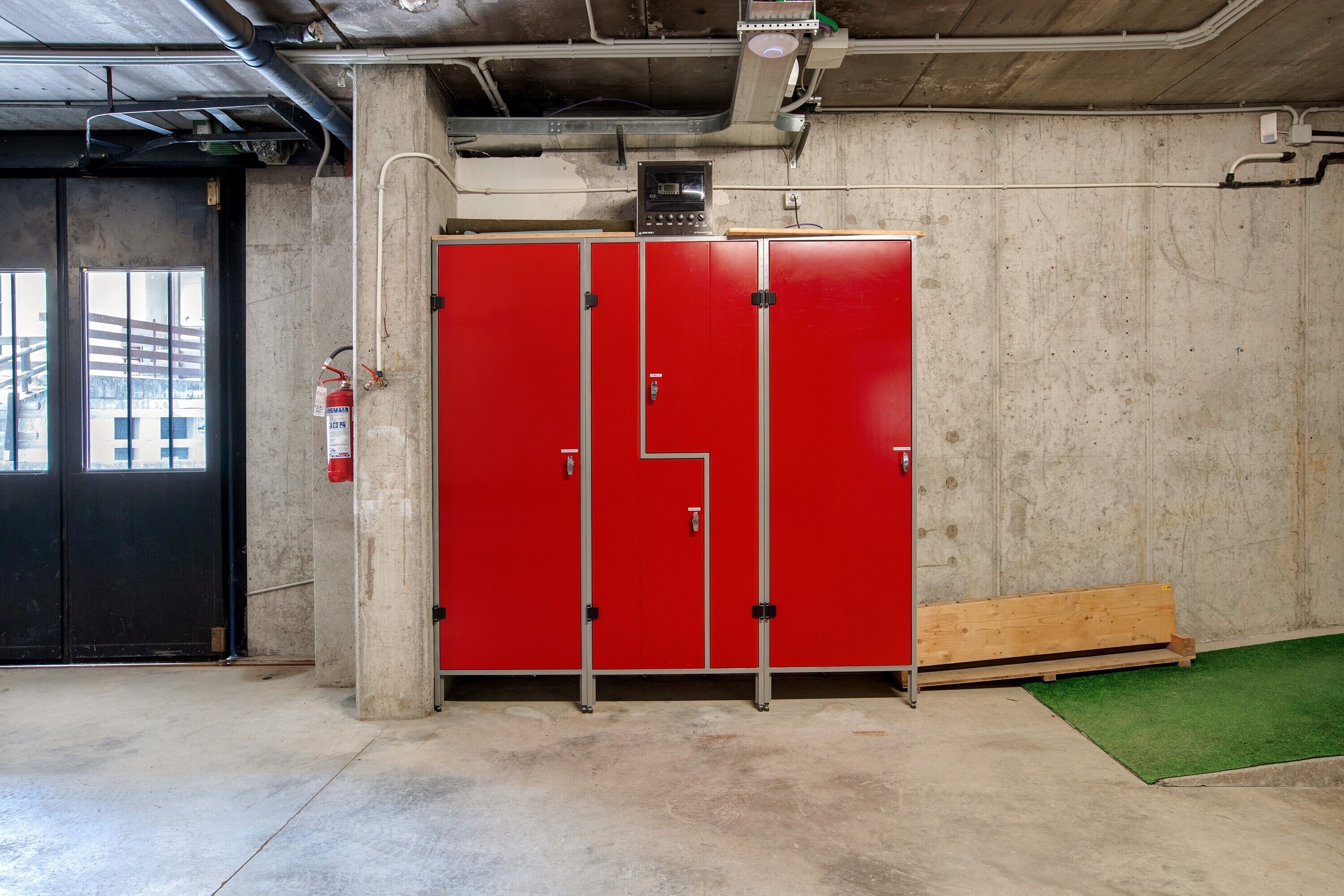 Un meuble de rangement rouge, muni d’un extincteur et d’un panneau de commande fixés au mur.
