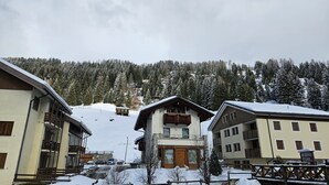 A snow-covered mountain village with multi-story buildings, a ski lift, and a forested backdrop.
