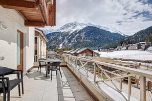 Een balkon met uitzicht op besneeuwde bergen, een houten hekwerk en een tafel met stoelen.