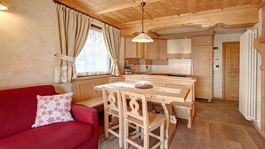 A cozy cabin interior with a wooden dining table, a red sofa, and a kitchen area. - Apartment 'Genziana' with Mountain View, Private Terrace and Wi-Fi (Santa Caterina)