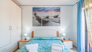 Un dormitorio con cama, dos mesitas de noche, un armario y un cuadro grande de barcos en la pared.