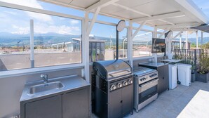 Cocina exterior con parrilla a gas, horno, pileta y vistas a montañas distantes.