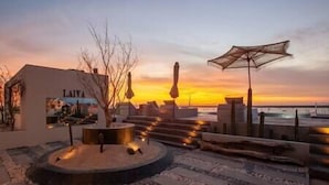 Een zonsondergang uitzicht vanaf een terras met een zwembad, ligbedden en een restaurant genaamd "LAIVA".