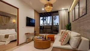 Een moderne hotelkamer met een bed, een bank, een salontafel en een groot raam met uitzicht op palmbomen.
