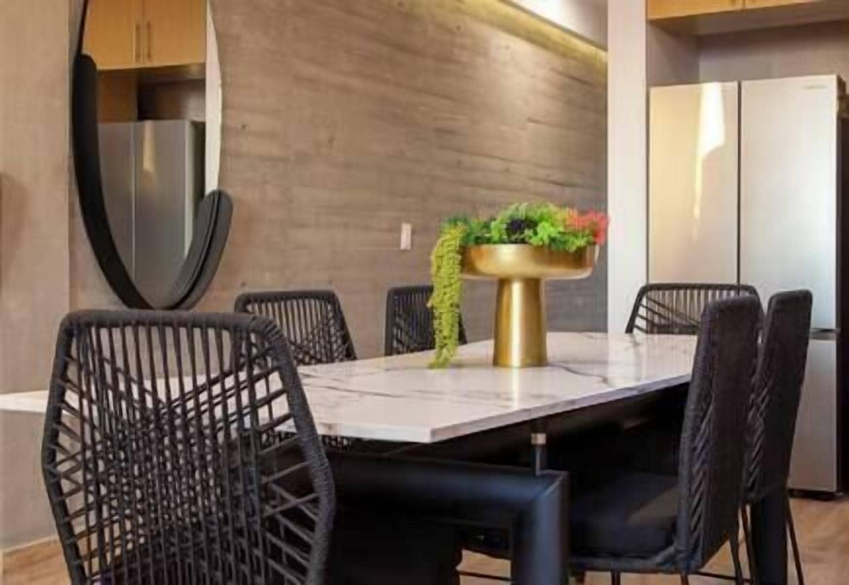 A modern dining area with a marble table, black wireframe chairs, and a gold pedestal with a plant.