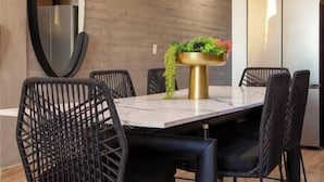 Een moderne eethoek met een marmeren tafel, zwarte draadframe stoelen en een gouden voetstuk met een plant.