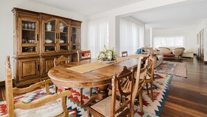 Un comedor con mesa de madera, sillas, un armario con puertas de vidrio y un sofá al fondo.
