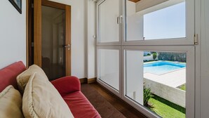Habitación con sofá rojo, puerta de cristal que da al exterior y vista a una piscina.