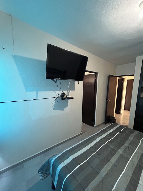 A bedroom with a bed, a flat-screen TV mounted on the wall, and a door leading to another room.