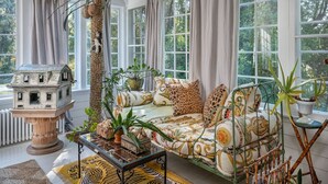 Een gezellige woonkamer met een gestreept sofa, een decoratief huismodel en verschillende planten.