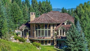 Una casa grande de varios pisos con fachada de piedra, ventanas amplias y un porche envolvente.