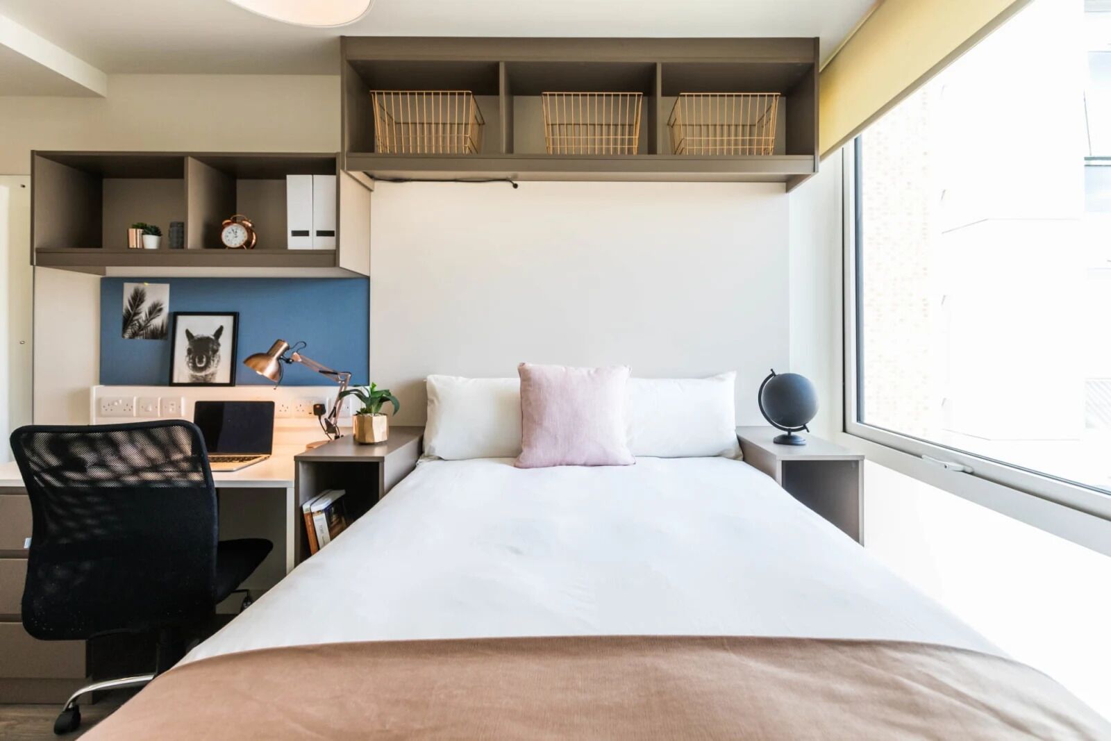 Une chambre d’hôtel moderne avec un grand lit, un bureau avec un ordinateur portable, une chaise et une fenêtre donnant sur la ville.
