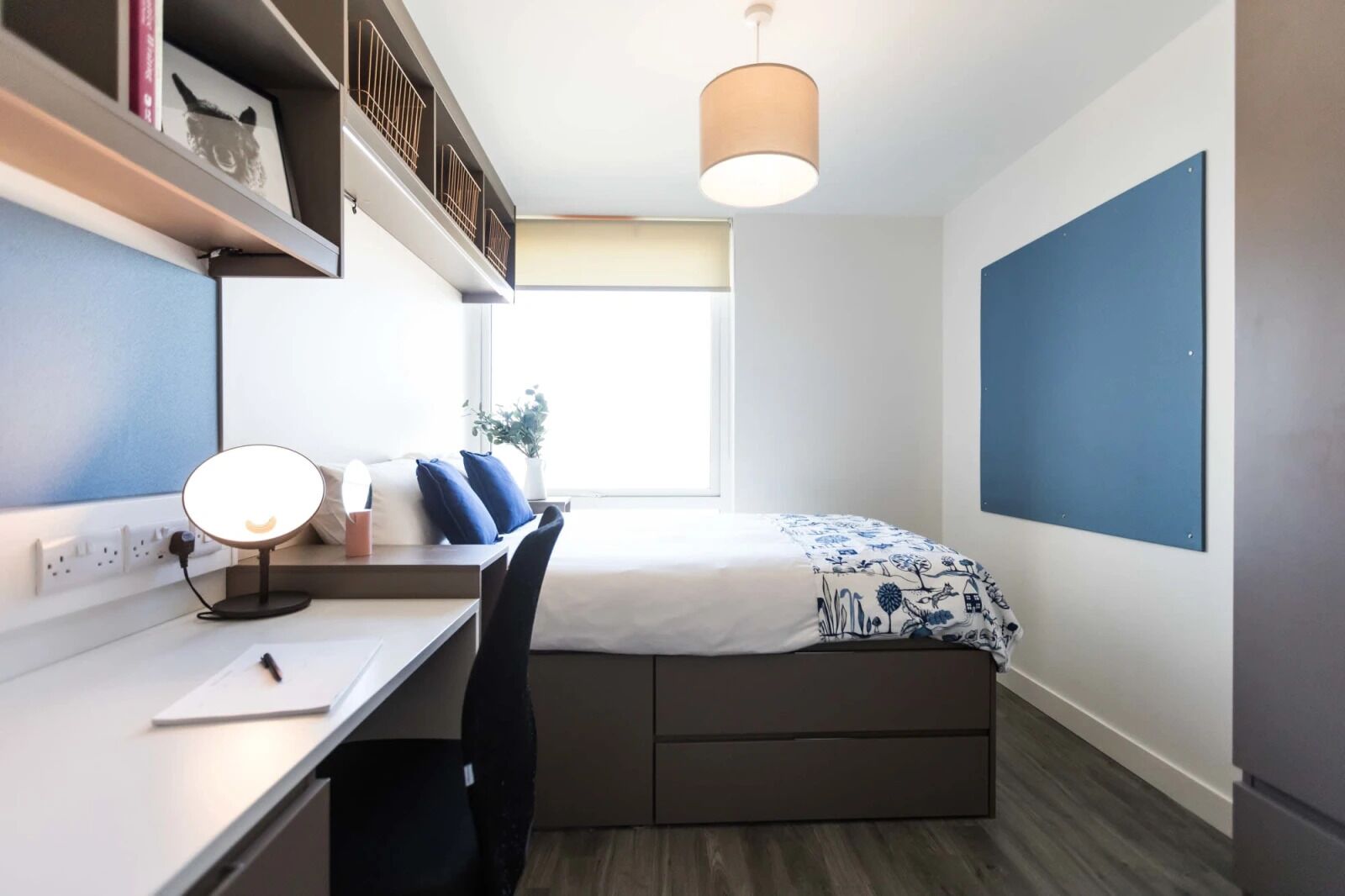 Un dormitorio pequeño con cama, escritorio, silla y lámpara colgante.