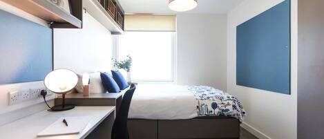 Un dormitorio pequeño con cama, escritorio, silla y lámpara colgante.