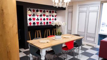 Un coin repas avec une table en bois, des chaises noires et rouges, un lustre et un mur décoré de motifs de cartes à jouer.