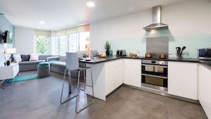A modern kitchen with white cabinets, a stainless steel range hood, and a built-in oven. - Student Only Arbury Court in Kingston (New Malden)