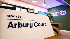A reception desk with a sign reading "aperto Arbury Court" and a neon sign in the background. - Student Only Arbury Court in Kingston (New Malden)
