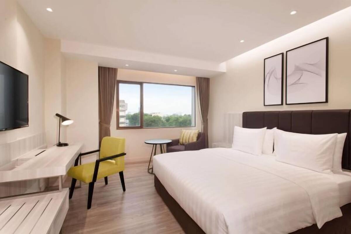 A hotel room with a bed, a desk, a chair, a TV, and a window.