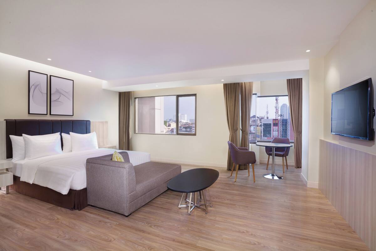 A modern hotel room with a bed, a sofa, a dining table with chairs, and a TV.
