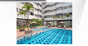 A swimming pool with lounge chairs and umbrellas, surrounded by a building with multiple floors and balconies. - AIHO Hotel Medan  (Medan)