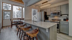 Een moderne keuken met een groot kookeiland, barstoelen, roestvrijstalen apparatuur en uitzicht op besneeuwde bomen door grote ramen.