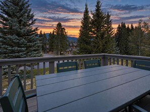 Una terraza con mesa y sillas, con vistas a un área boscosa y un atardecer de fondo.